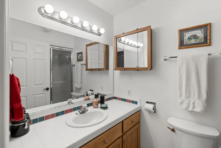Vanity featuring a single basin sink, oak-finish cabinetry, and a tile countertop with decorative accent trim