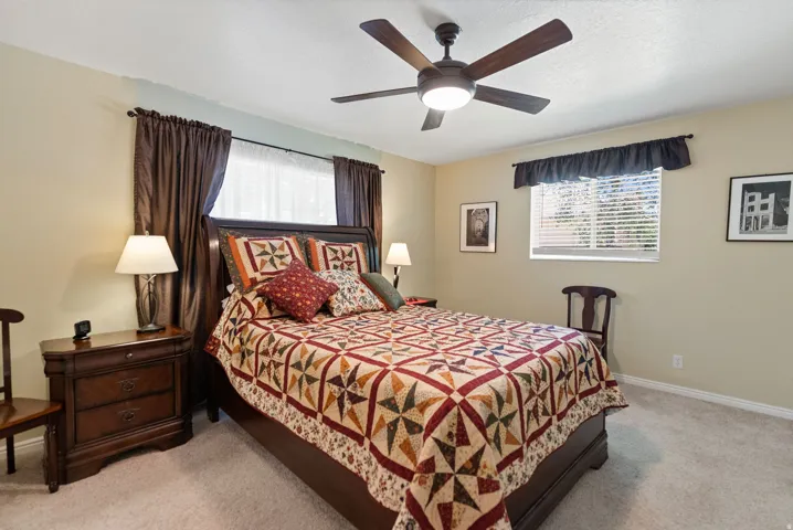 Primary bedroom with neutral-toned walls, light carpet flooring, and a ceiling fan with integrated lighting