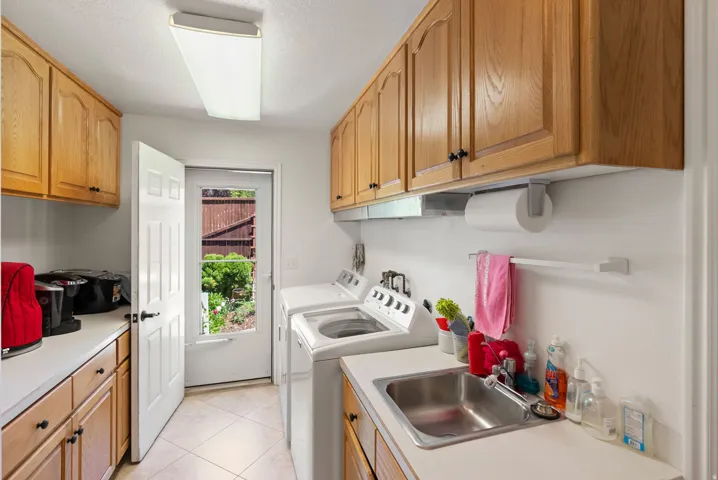 Utility room featuring light wood cabinetry, white countertops, tile flooring, and a stainless steel sink