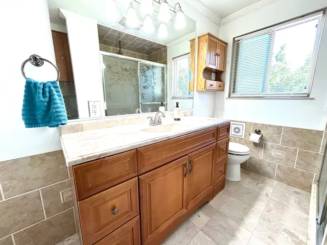 Spacious bathroom featuring a dual vanity with a light-toned countertop, wood-finish cabinetry, and a large mirror