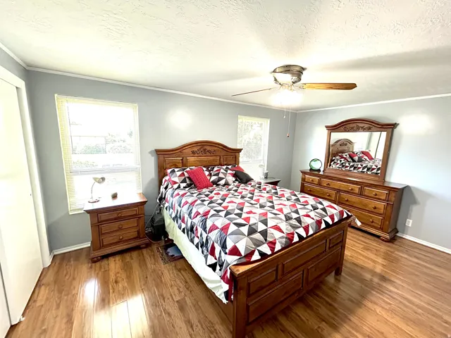 Spacious room featuring wood-finish flooring, two window openings with blinds, a ceiling fan fixture, and light gray wall tones