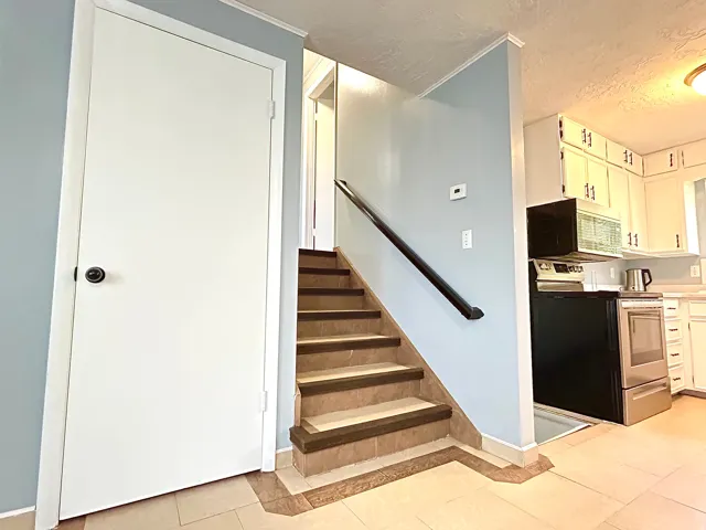 Tiled flooring extending to the staircase featuring a dark wood-finish handrail, light blue wall paint, and white trim