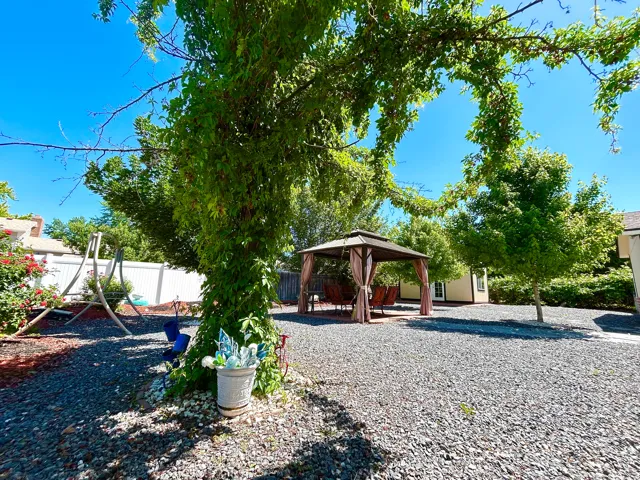 Private outdoor space featuring a covered gazebo, mature trees, gravel ground cover, and a white perimeter fence