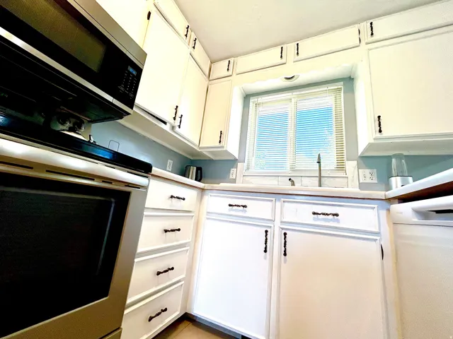 Kitchen featuring white cabinetry with dark hardware, a stainless steel over-the-range microwave, and a window with horizontal blinds