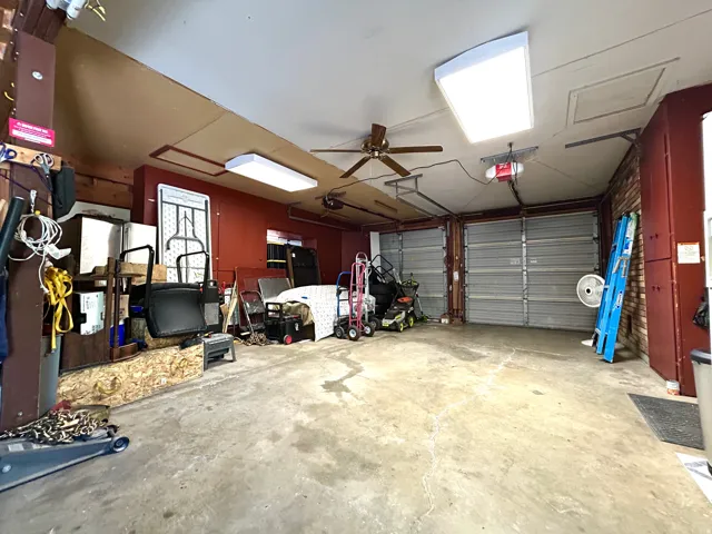 Concrete floor garage featuring two roll-up garage doors, a ceiling fan, and fluorescent lighting