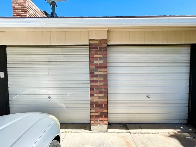 Two-car garage featuring white horizontal panel doors and a brick pillar