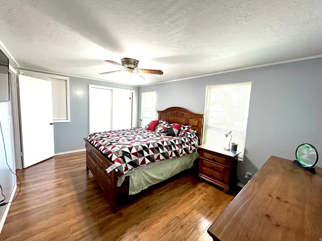 Bedroom featuring wood-finish flooring, light gray walls, a ceiling fan with integrated lighting, and multiple windows