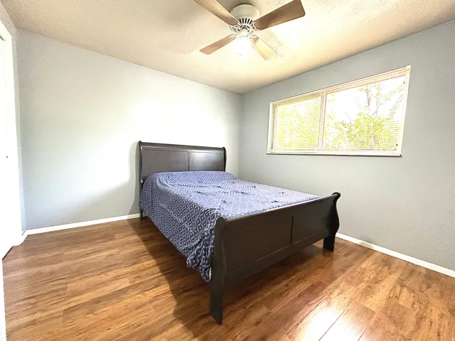 Bright room featuring wood-finish flooring, a ceiling fan with integrated lighting, and a large window