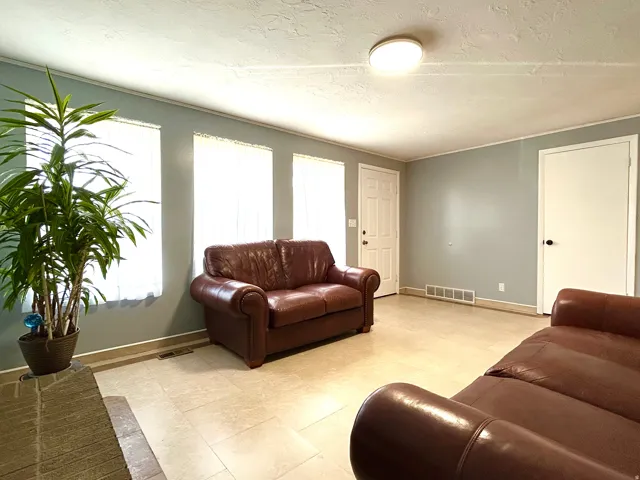 Living space featuring light-toned tile flooring, three vertical windows with sheer coverings, and a white paneled entry door