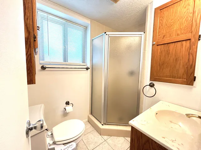 Bathroom featuring a corner shower with frosted glass enclosure, a vanity with an integrated sink, a commode, and tiled flooring