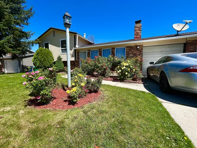 Front exterior featuring brick and siding finishes, an attached garage, a concrete driveway, and a landscaped yard with flowering shrubs and a decorative lamppost