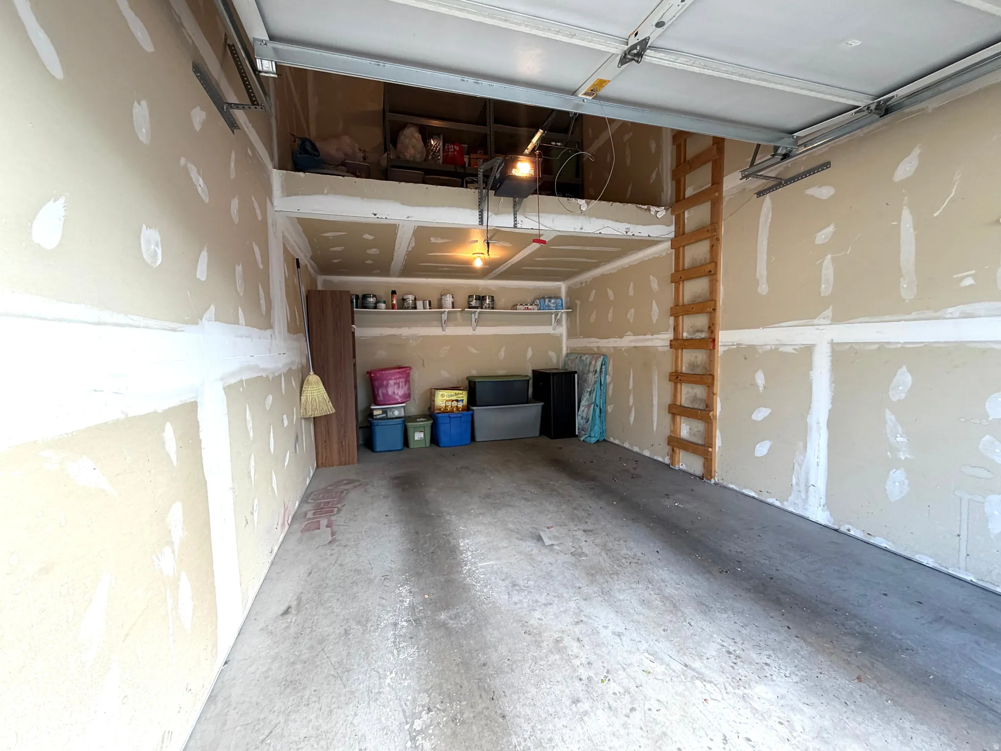Spacious garage with concrete flooring, overhead garage door, built-in shelving, and an elevated storage platform