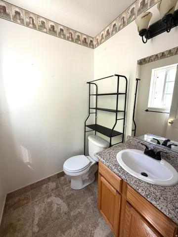Bathroom featuring a wooden vanity with a granite-style countertop, an oval sink with a black faucet, a wall-mounted mirror, and tiled flooring