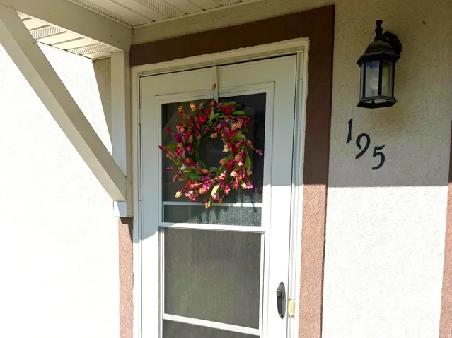 Front entry featuring a white storm door, stucco exterior, exterior wall lantern, and concrete entryway