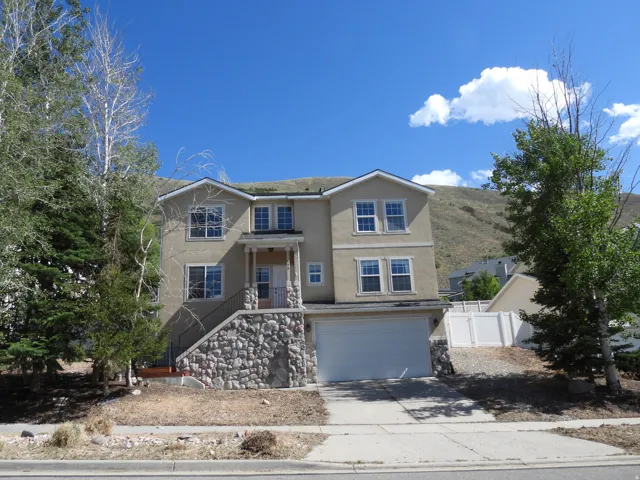 Multi-level residence featuring a stucco exterior with stone accents, a two-car garage, and a covered entry porch