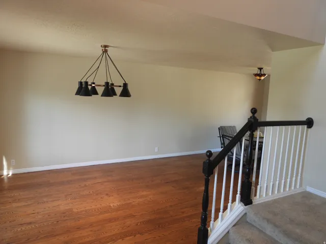 Spacious interior featuring wood-finish flooring, a contemporary six-light chandelier, and a staircase with a dark wood newel post and white balusters