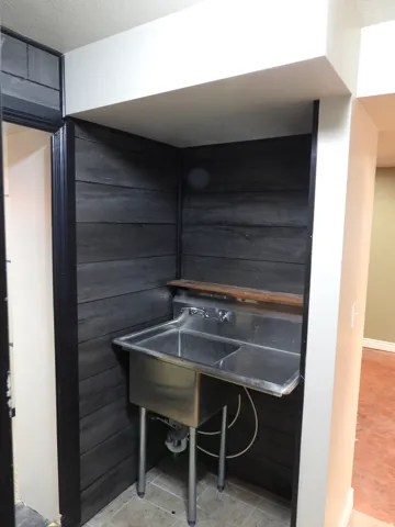 Utility sink with double basins and integrated countertop, set against horizontal dark wood-finish paneling