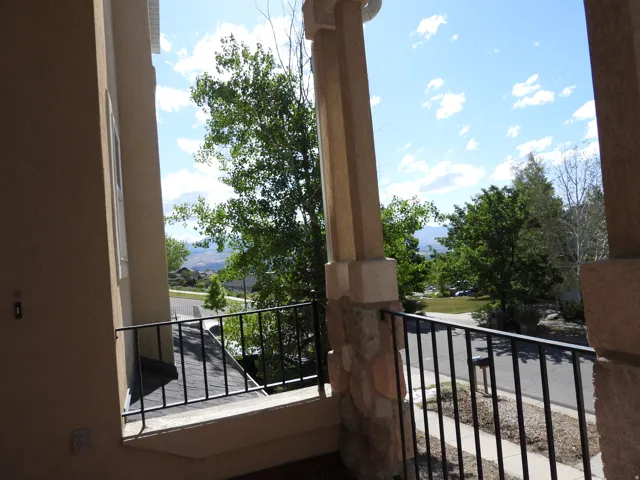 Inviting front porch featuring stone-clad columns, a wrought iron railing, and stucco siding