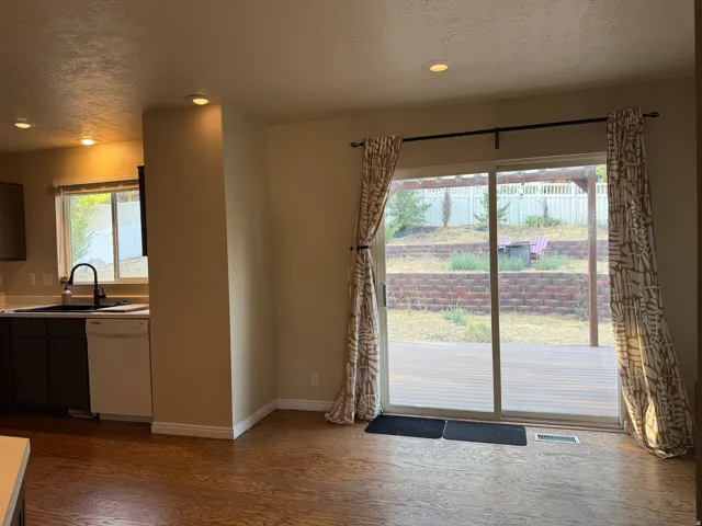 Sliding glass door to an outdoor deck, wood-finish flooring, recessed lighting, and a kitchen featuring a window and built-in dishwasher