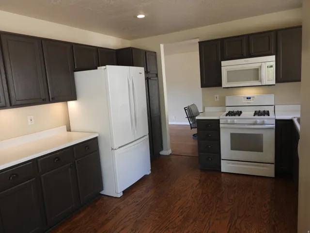 Kitchen featuring dark wood-finish cabinetry, white countertops, a gas range, an over-the-range microwave, and wood-finish flooring