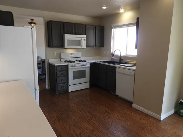 Kitchen featuring wood-finish flooring, dark cabinetry, white countertops, and a white appliance suite including a range and dishwasher