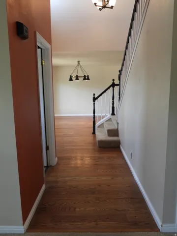 Hardwood flooring spanning the entryway, featuring a carpeted staircase with a dark wood handrail and white balusters