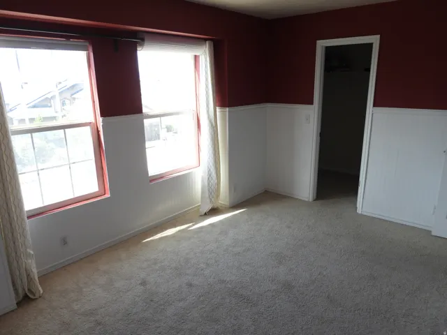 Carpeted room featuring two prominent windows with red trim, white beadboard wainscoting, and a doorway leading to an interior space