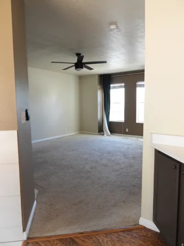 Spacious living area featuring neutral carpeting and a ceiling fan