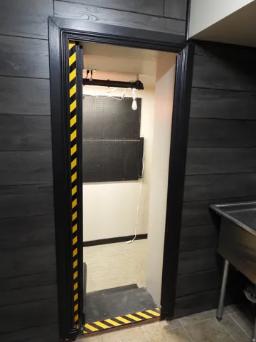 Entryway featuring black wood paneling, black trim with yellow and black hazard stripe accents, a utility sink, and a view into an interior room with a pegboard wall