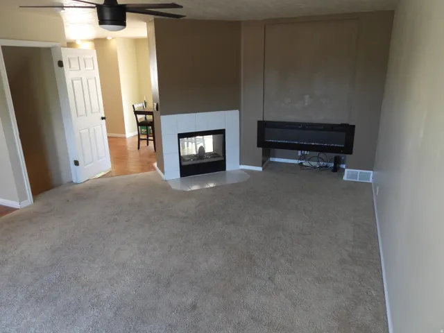 Carpeted living area featuring a built-in fireplace with a white tile surround and hearth