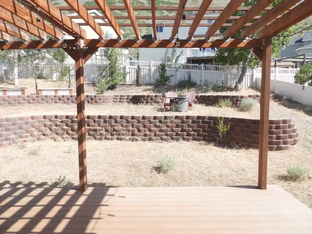 Spacious outdoor deck with a wood pergola, featuring decorative string lights, overlooking a tiered backyard with block retaining walls and a fenced perimeter