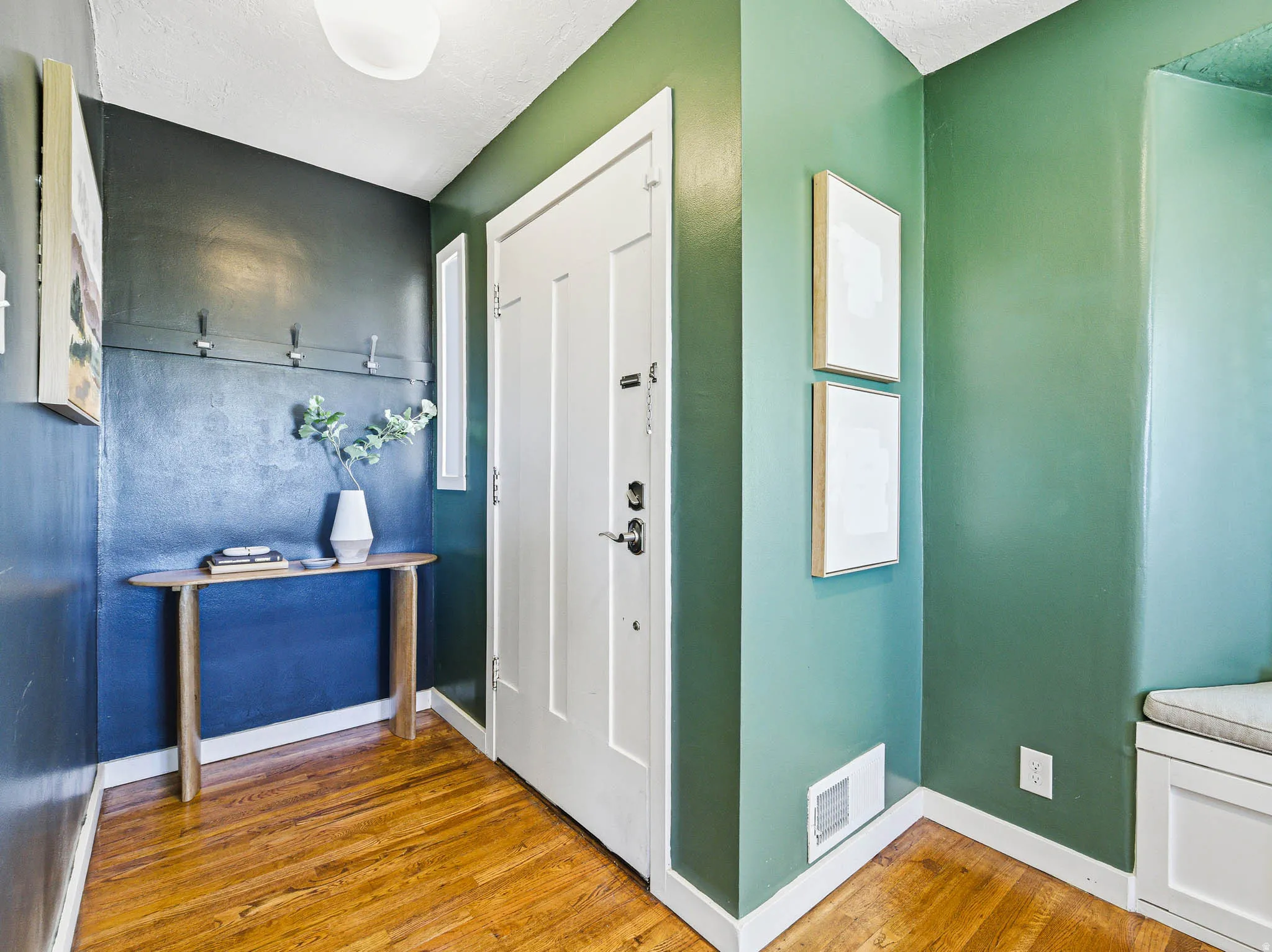 Entryway featuring wood-finish flooring, a white paneled door with dark hardware, a built-in bench with storage, and a wall-mounted coat rack