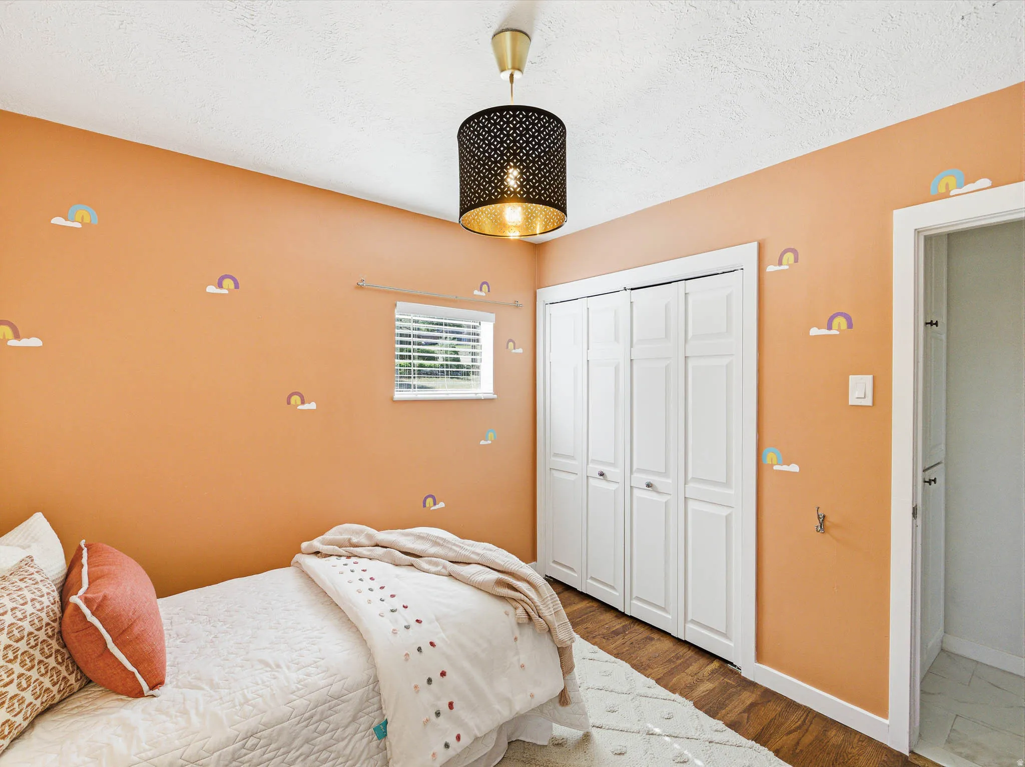 Spacious room featuring wood-finish flooring, a contemporary ceiling light fixture, a window with horizontal blinds, and paneled bi-fold closet doors