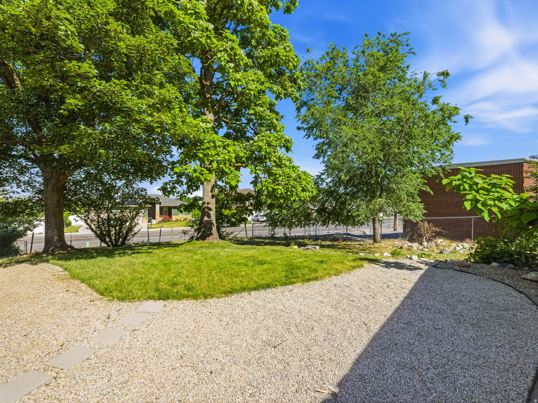 Landscaped yard featuring a gravel pathway, stone pavers, mature trees, and a manicured lawn