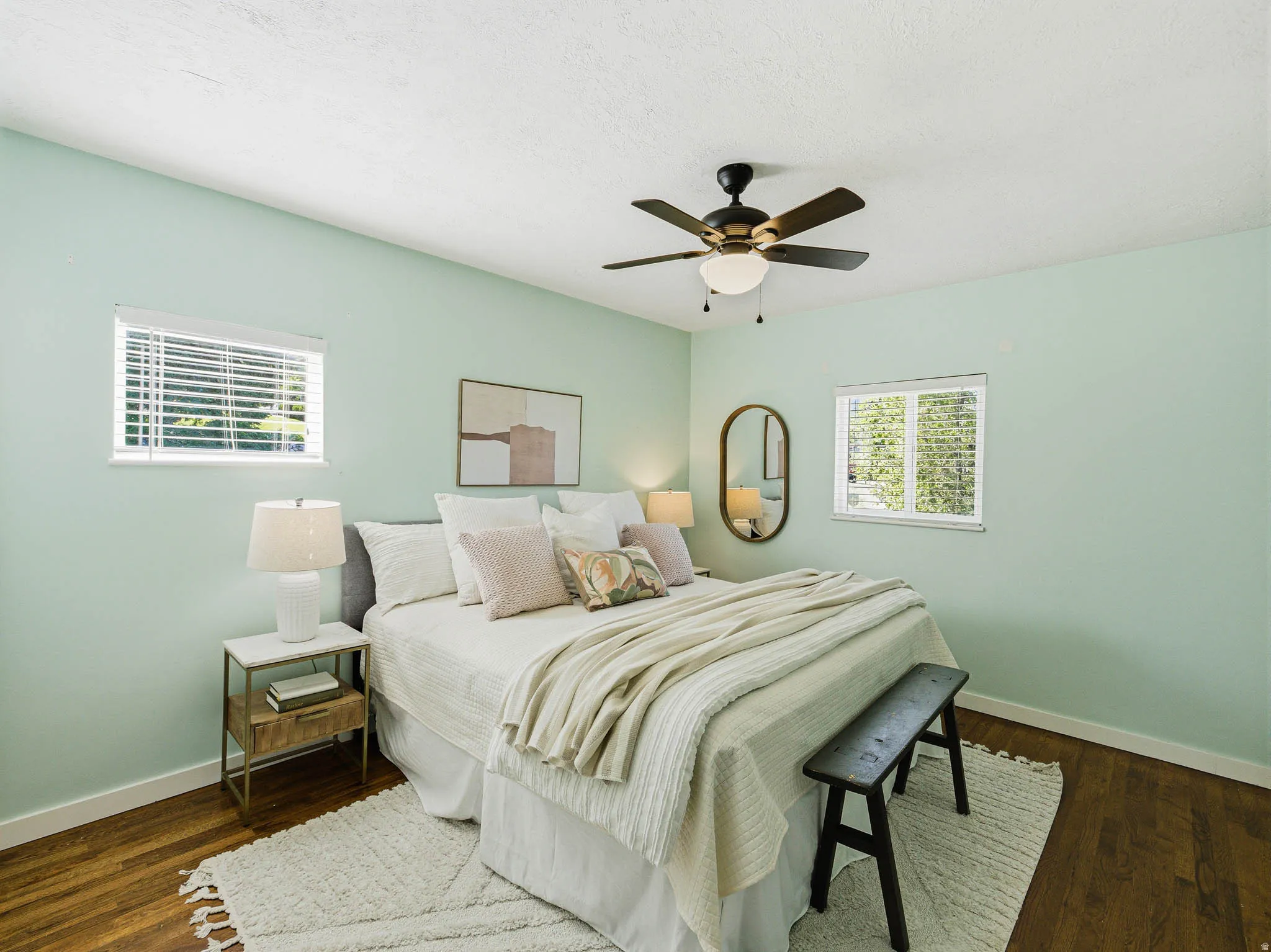 Bedroom featuring light green walls, wood-finish flooring, and two windows with blinds