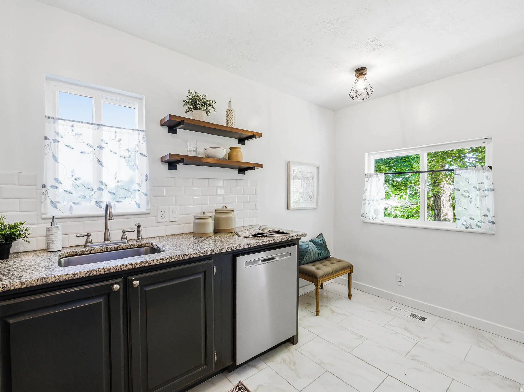 Kitchen area featuring dark cabinetry with silver hardware, speckled countertops, a stainless steel sink, and a white subway tile backsplash