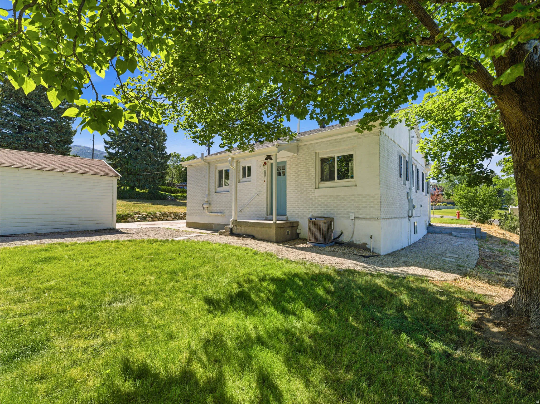 Rear white brick exterior featuring a light blue entry door, concrete patio, and a grass lawn