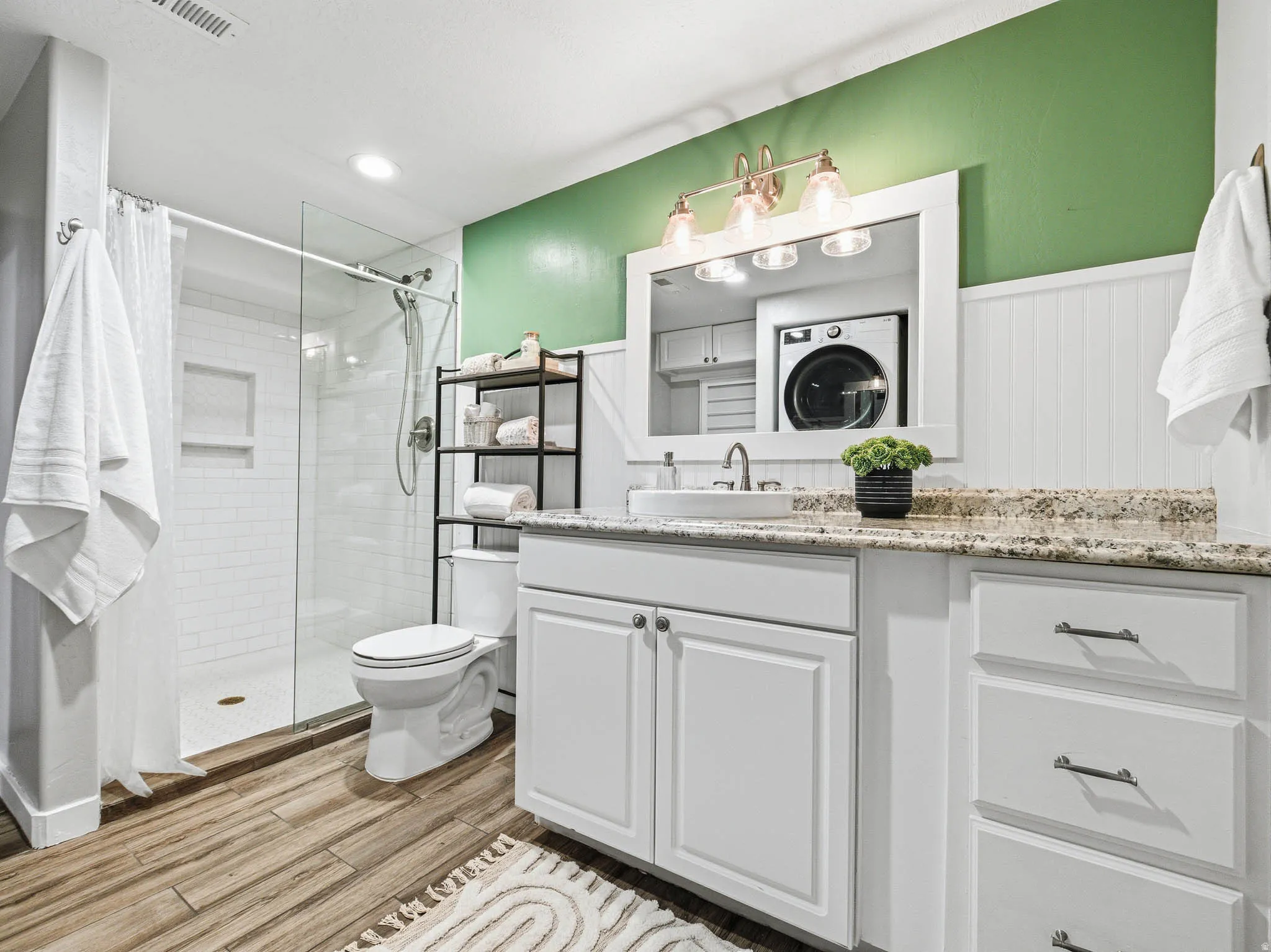 Bathroom featuring a glass-enclosed shower with subway tile, wood-finish flooring, a vanity with white cabinetry, granite-finish countertop, and a vessel sink