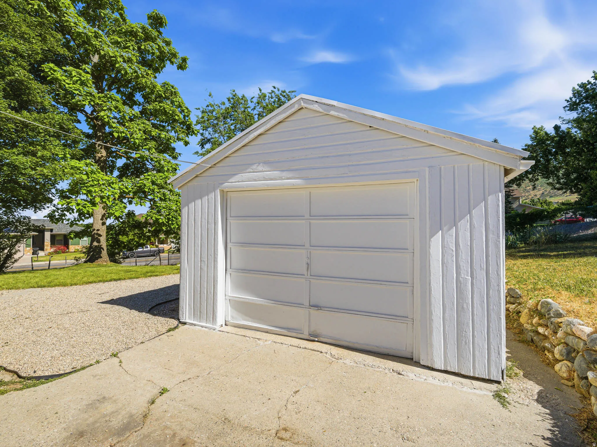 Detached garage with a single panel door, white vertical siding, and a gabled roof