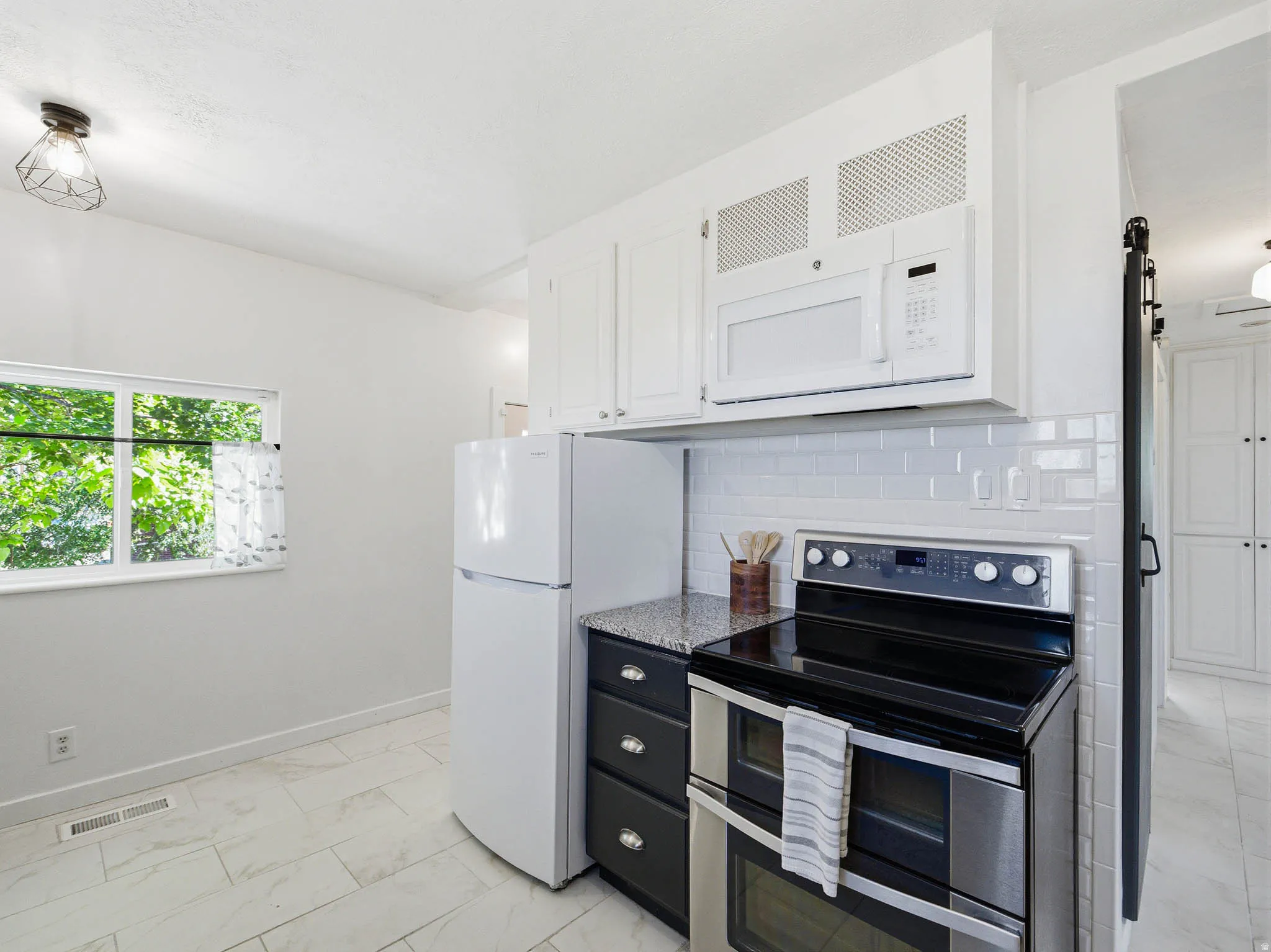 Kitchen featuring white cabinetry, subway tile backsplash, granite-style countertops, stainless steel appliances, and tile flooring