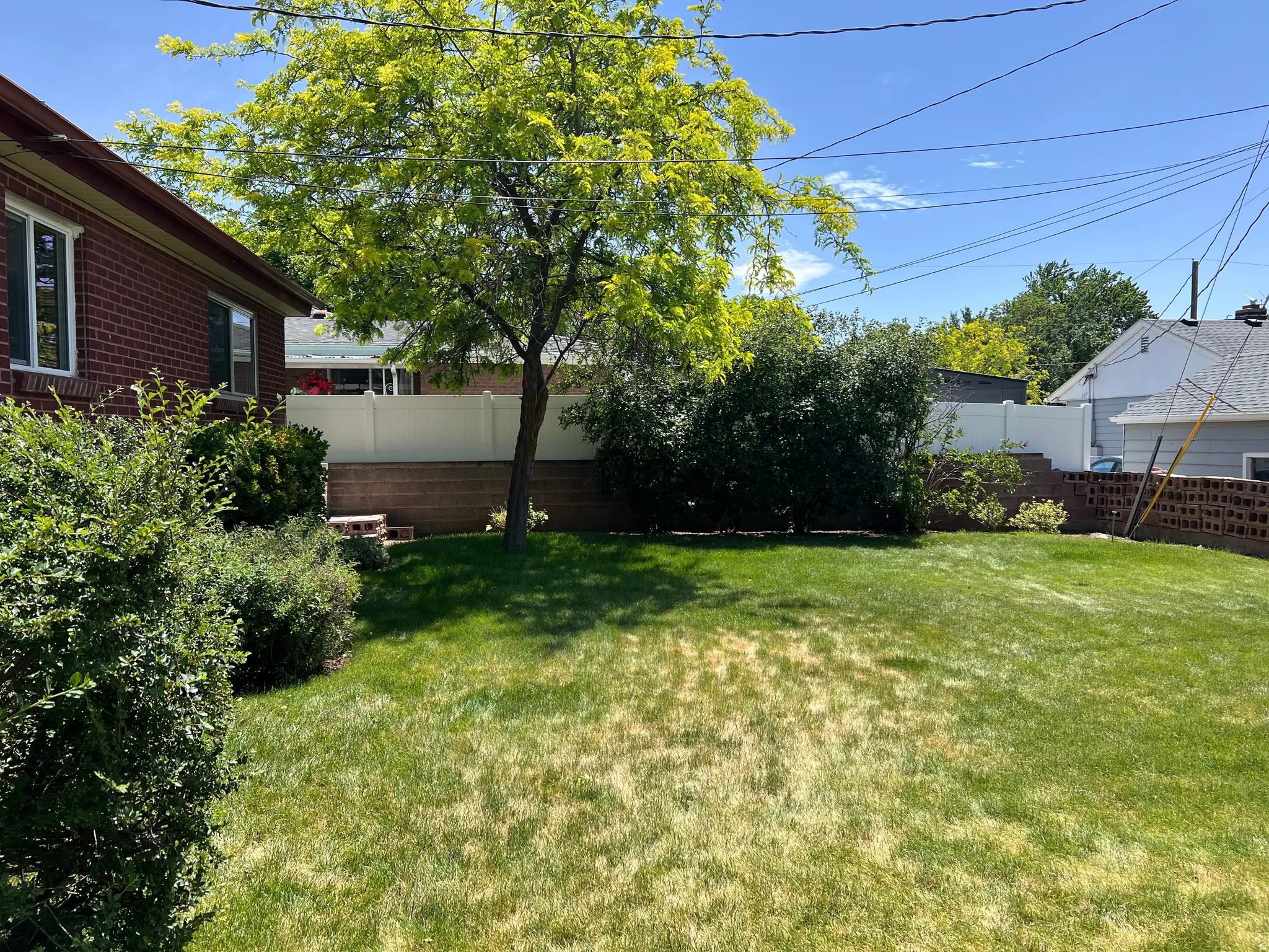 Expansive green lawn with mature landscaping, a privacy fence, and brick retaining walls