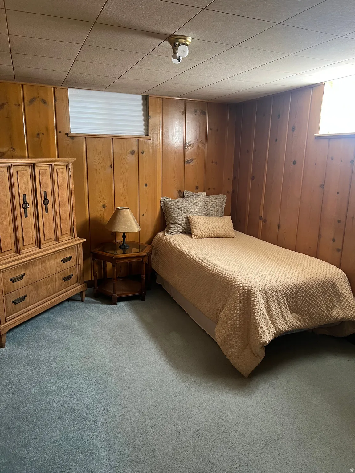 Room featuring wood paneling, blue carpeting, and a drop ceiling
