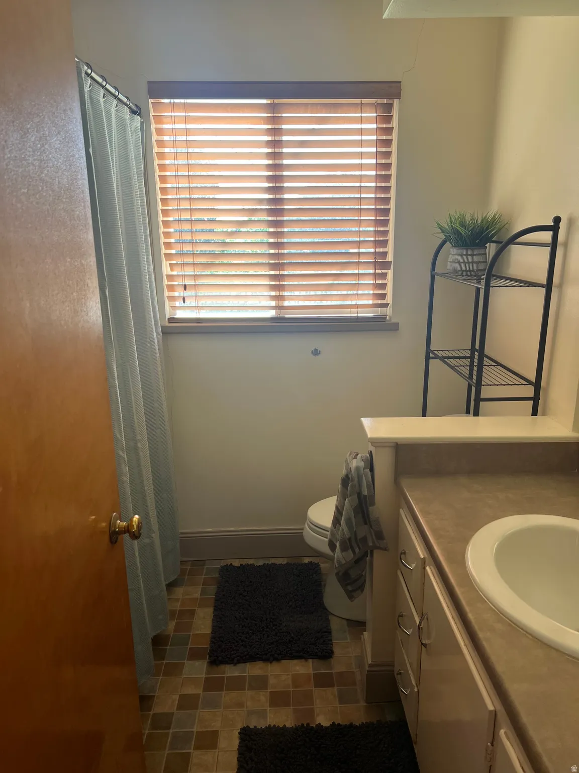 Bathroom featuring a window with wood-finish blinds, a vanity with an integrated sink and base cabinetry, patterned floor tiles, and a built-in toilet