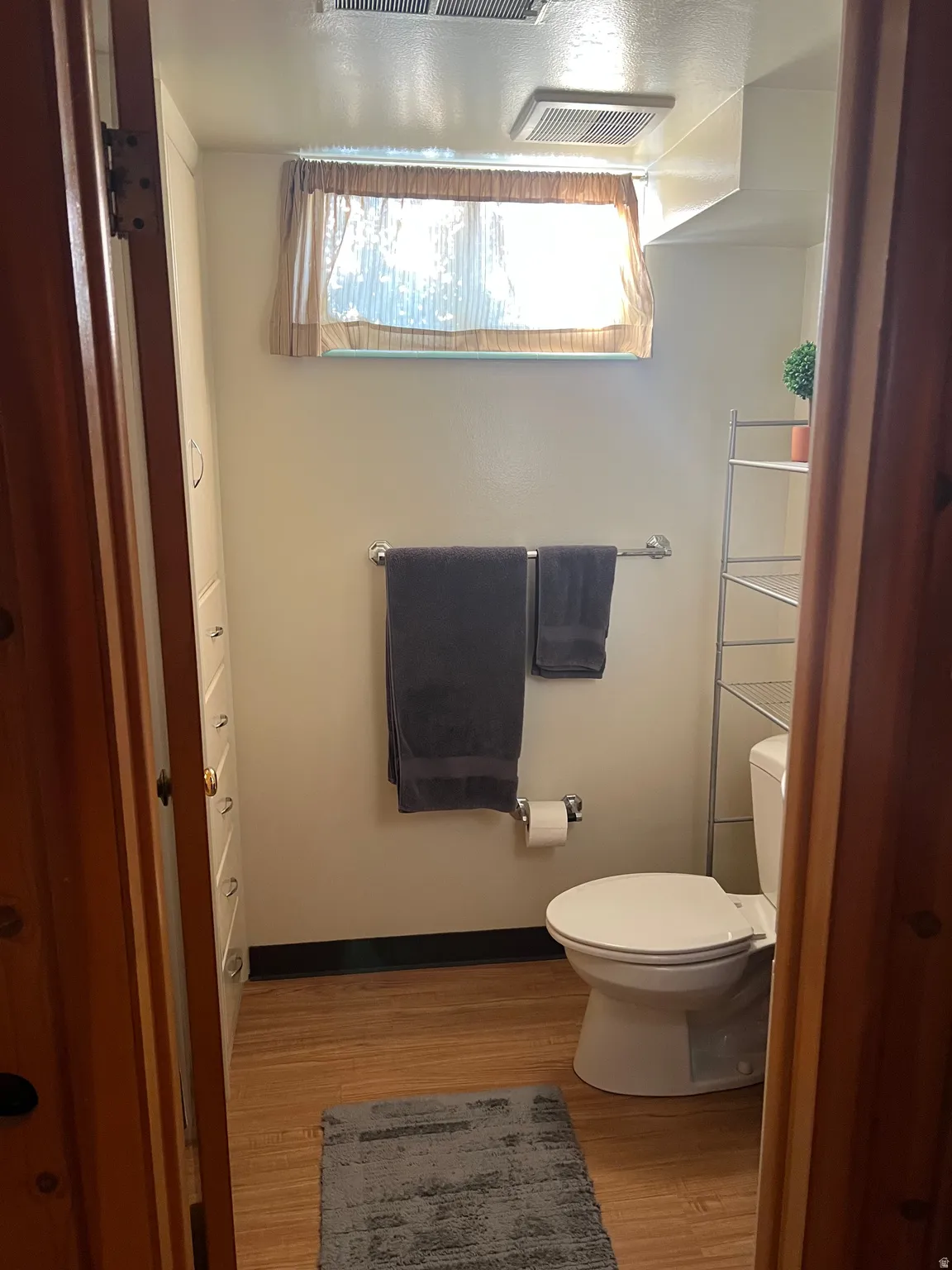 Full bathroom featuring wood-finish flooring, a white toilet, and a built-in storage cabinet with multiple drawers