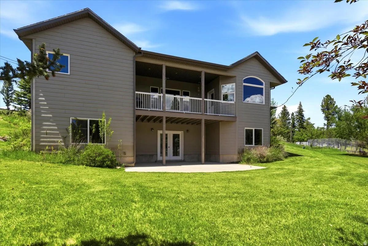 Expansive green lawn bordering a two-story home with a covered lower patio and an upper-level balcony, lower-level patio, and multiple windows including an arched upper window