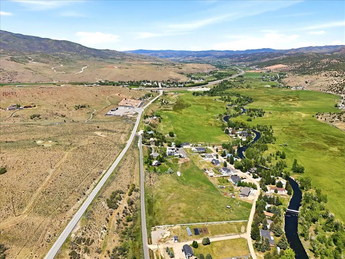Expansive aerial showcasing a valley landscape with a winding river, scattered residential properties, and distant mountains