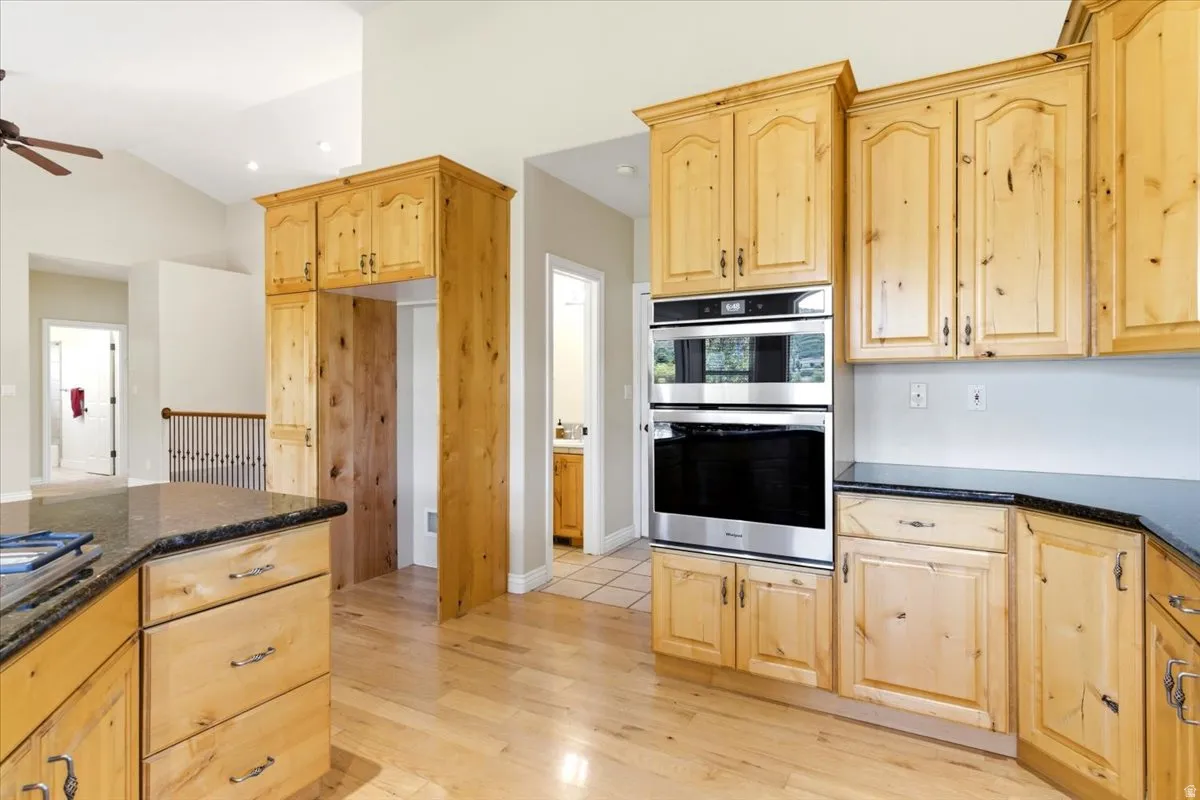 Kitchen featuring extensive knotty alder cabinetry, dark granite countertops, stainless steel double wall ovens, built-in refrigerator enclosure, and wood-finish flooring