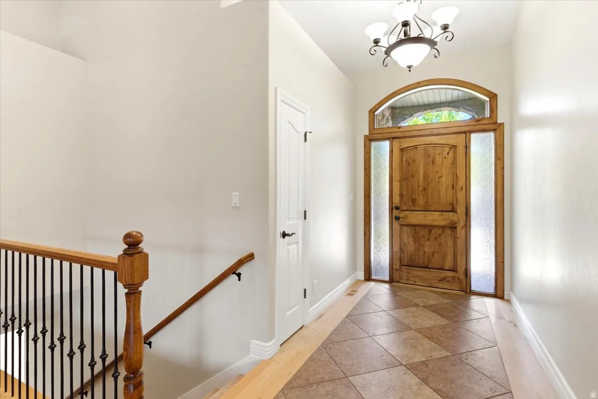 Foyer featuring a wood-finish entry door with arched transom and sidelights, overhead chandelier, and patterned tile flooring