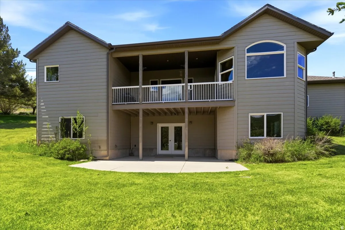 Rear exterior with a spacious concrete patio, a covered upper-level balcony with white railings, and a large arched window
