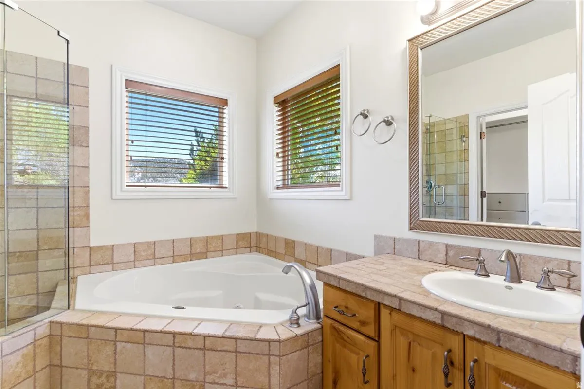 Bathroom featuring a corner soaking tub with tile surround, a glass-enclosed shower, wood-finish vanity with an undermount sink, and a framed mirror